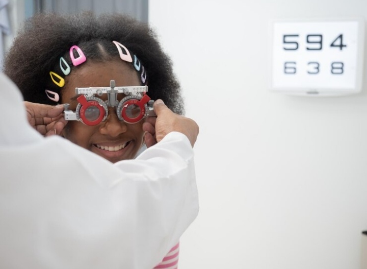 Optometrist conducting an eye exam on a young child using an eye chart with colorful shapes.