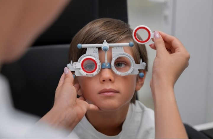 Optometrist conducting an eye exam on a young child using an eye chart with colorful shapes.