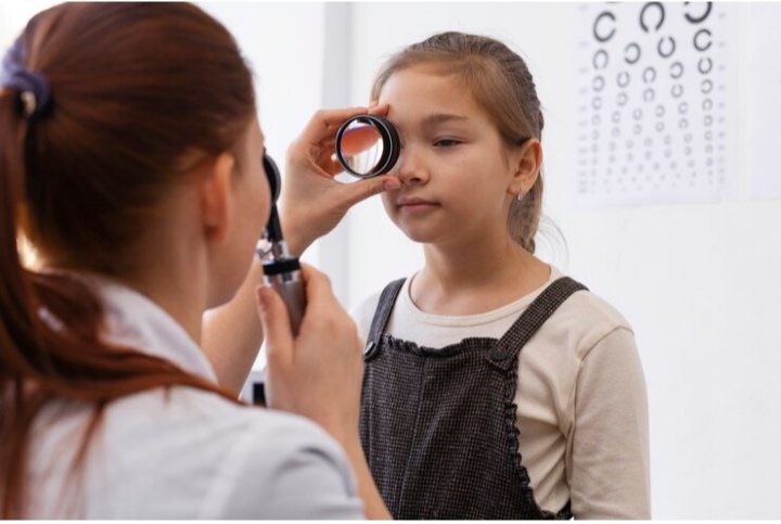 Optometrist conducting an eye exam on a young child using an eye chart with colorful shapes